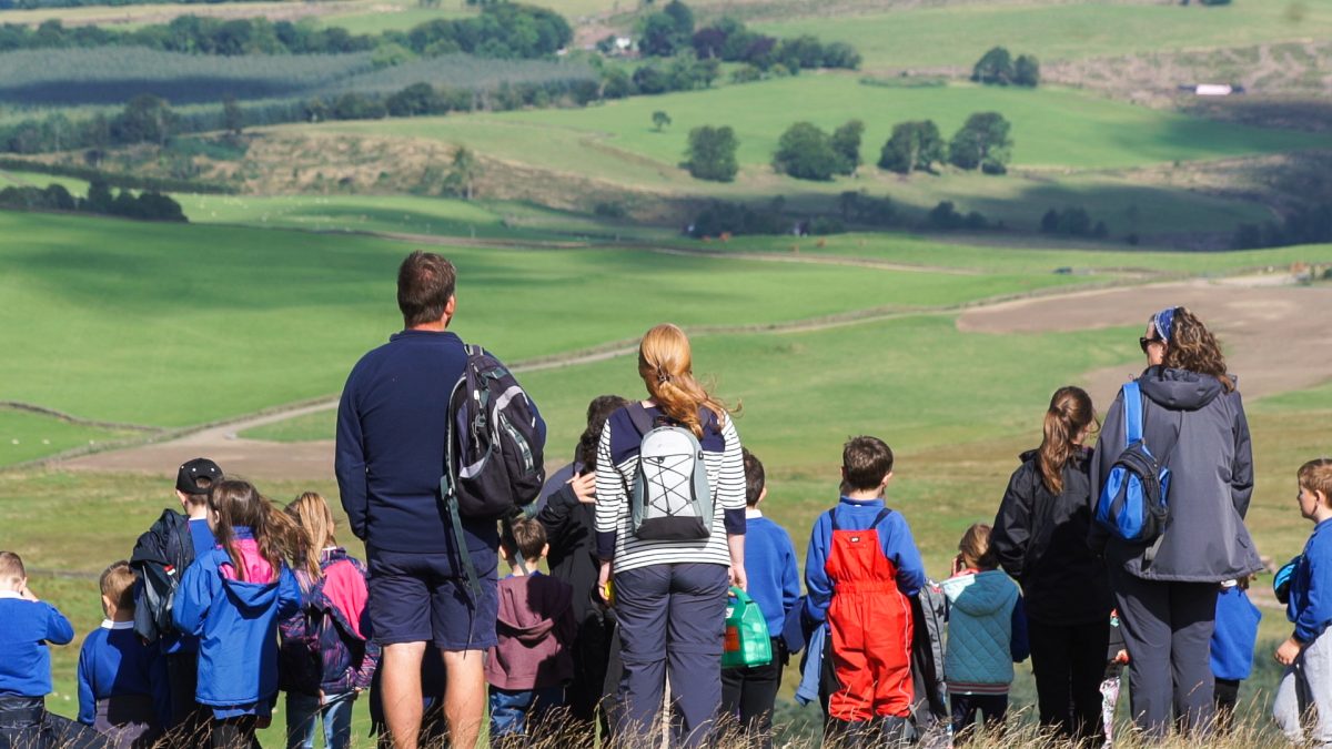 A group of adults and schoolchildren overlooking green fields.