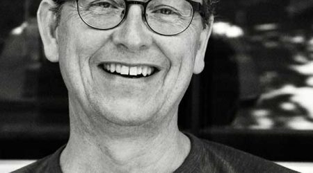 Black and white image of John Reid, a man wearing glasses.