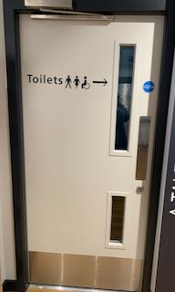 White door with two glass panels and a sign on the that reads 'Toilets' with an arrow.