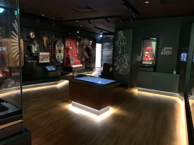 View of the museum gallery, with an interactive touch screen in the centre and cases with artefacts surrounding.
