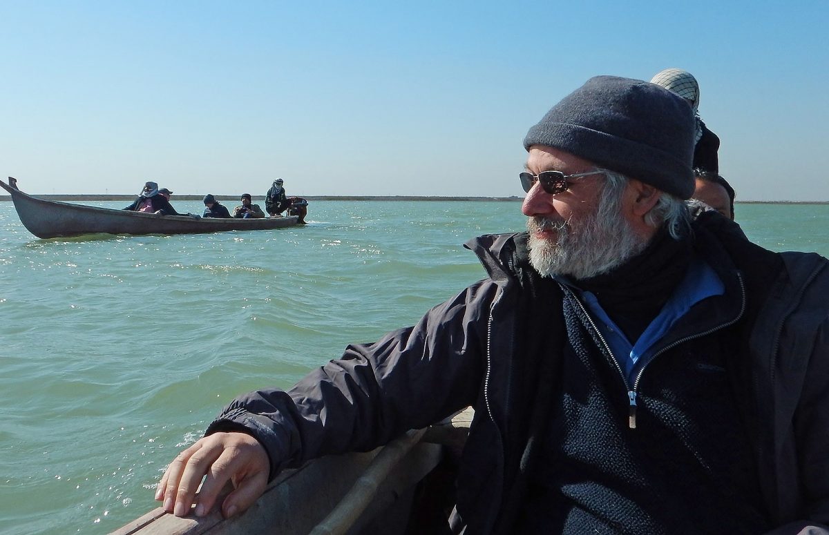 Man with grey beard sits in a boat wearing a grey beanie hat and sunglasses.