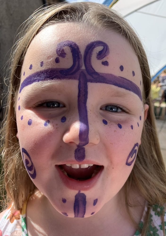 A girl wearing purple face paint in the style of an Iron Age person.